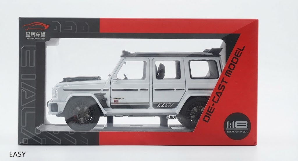 A 1:18 scale die-cast model of a silver Mercedes-Benz G-Class SUV, shown inside its red and black packaging box against a white background.
